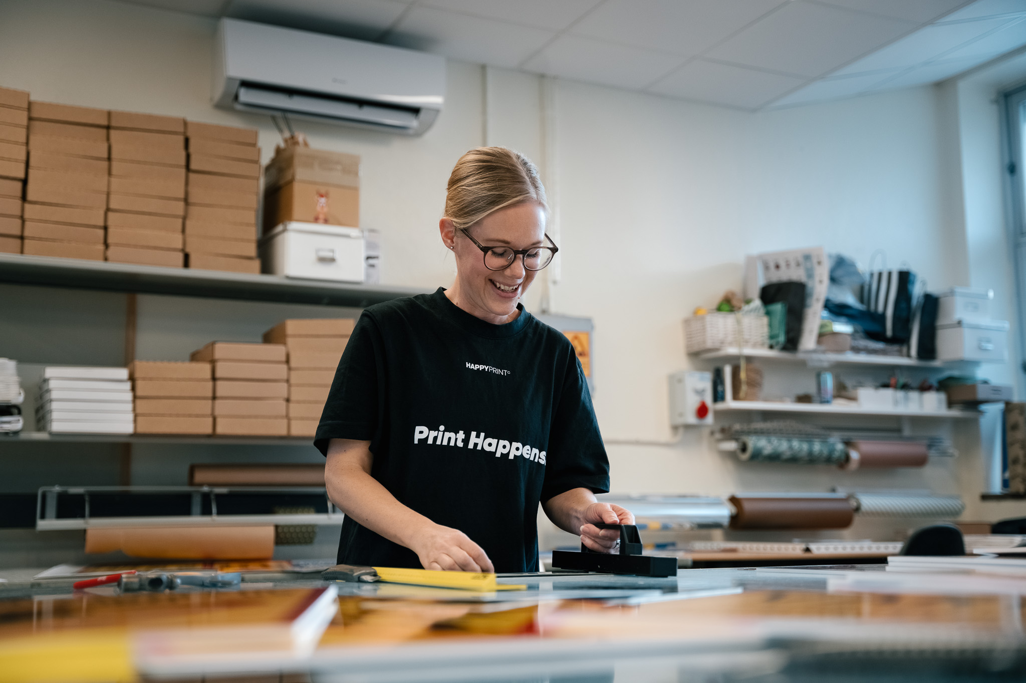 Leende kvinna som granskar tryckta skyltar i Happy Prints verkstad.