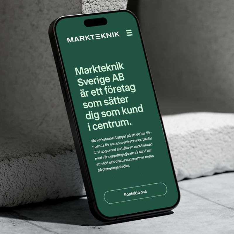 En smartphone som visar Marktekniks hemsida i mobilversion med företagets logotyp, en mörkgrön bakgrund och rubriken ”Markteknik Sverige AB är ett företag som sätter dig som kund i centrum.”