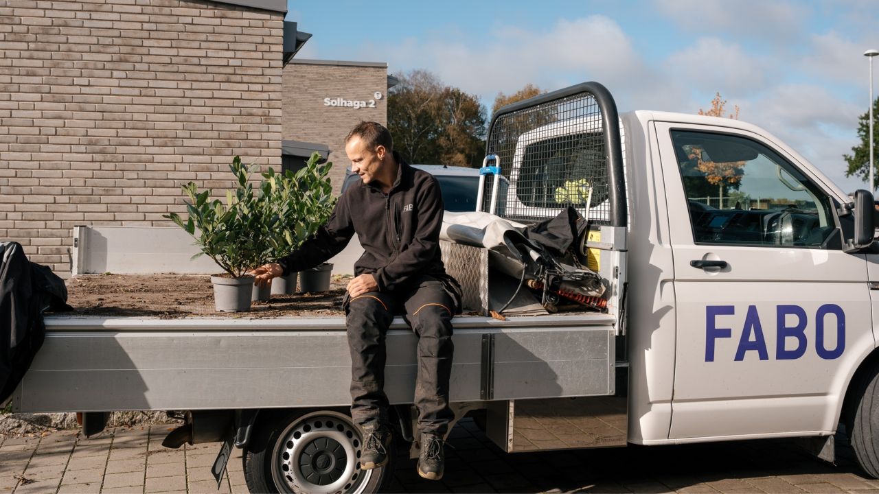 En medarbetare sitter på flaket till en Fabo-märkt arbetsbil och ser över krukväxter som ska planteras ut i bostadsområdet Solhaga.