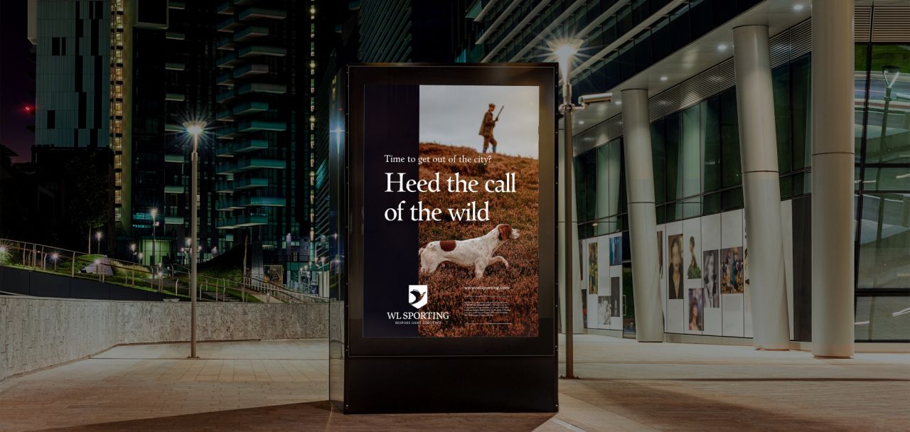 En digital reklampelare i en modern stadsmiljö som visar en annons för WL Sporting med rubriken ”Heed the call of the wild” och en bild på en jakthund i ett kargt naturlandskap.