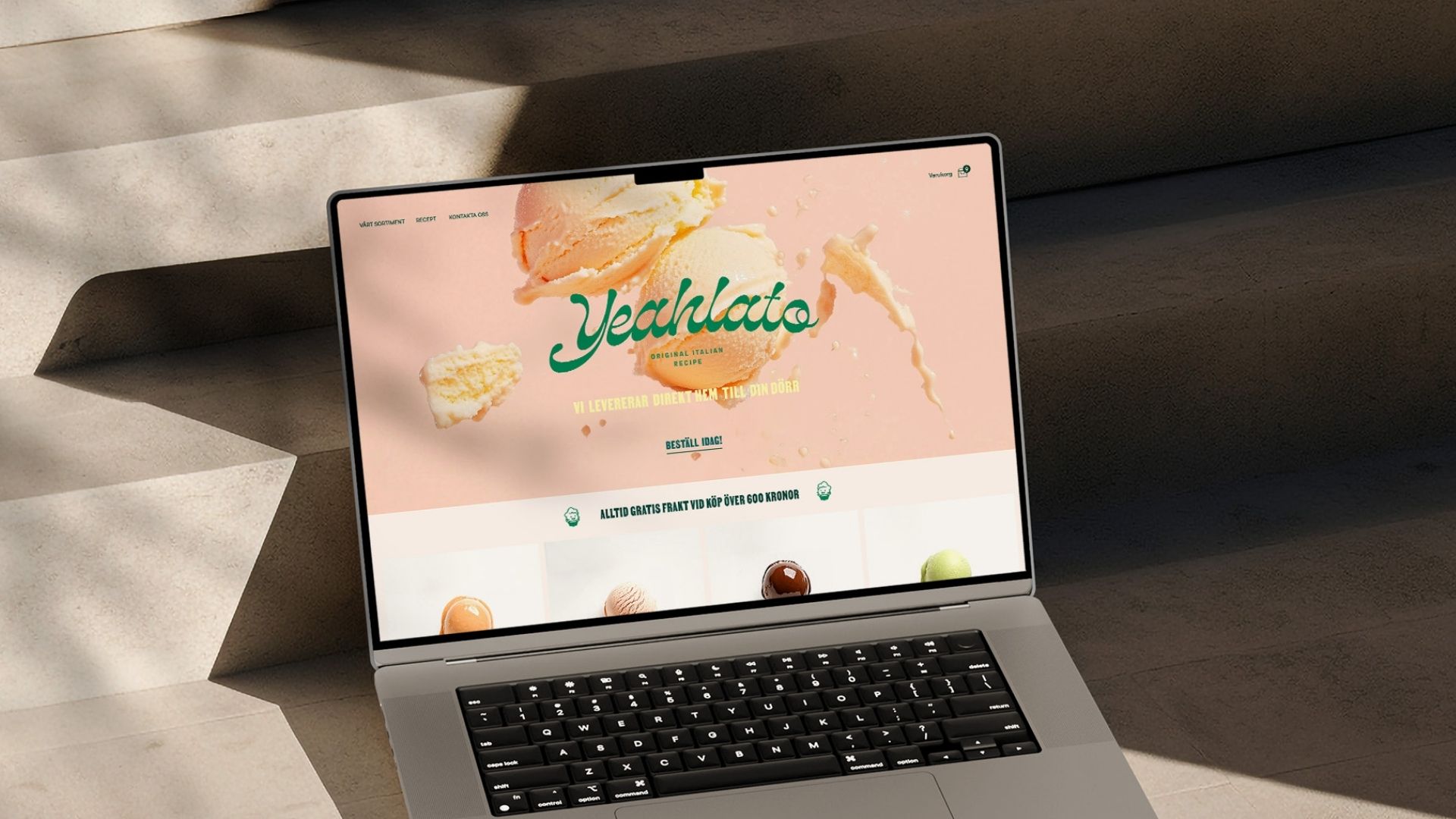  En laptop som visar Yeahlatos webbplats, där startsidan pryds av varumärkets lekfulla logotyp och aptitretande glasskulor mot en mjuk rosa bakgrund, i en miljö med naturliga skuggor.