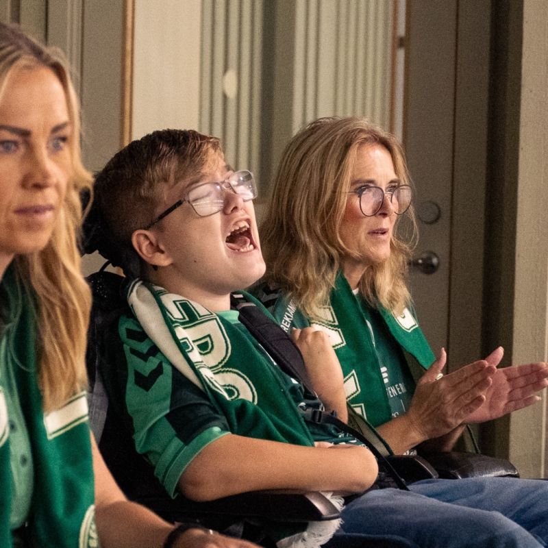  En engagerad ung supporter i HK Varberg-halsduk hejar passionerat från läktaren tillsammans med sin familj.