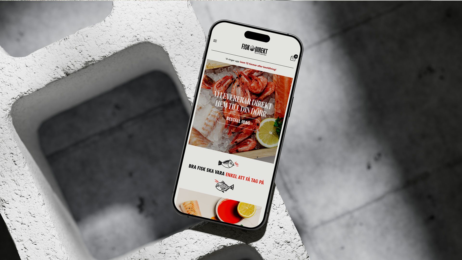En smartphone som visar Fisk Direkts nya hemsida i mobilversion med rubriken ”Vi levererar direkt hem till din dörr” över en bild på färska skaldjur. 