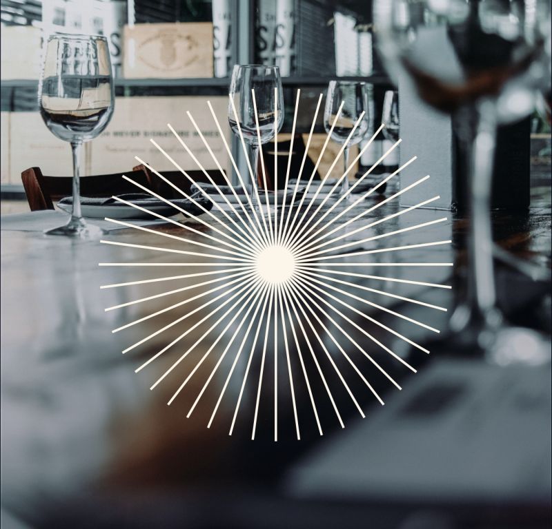  Ett stiliserat mönster av strålar från Societéns grafiska identitet överlagrat på en stämningsfull bild av dukade vinglas i restaurangmiljö