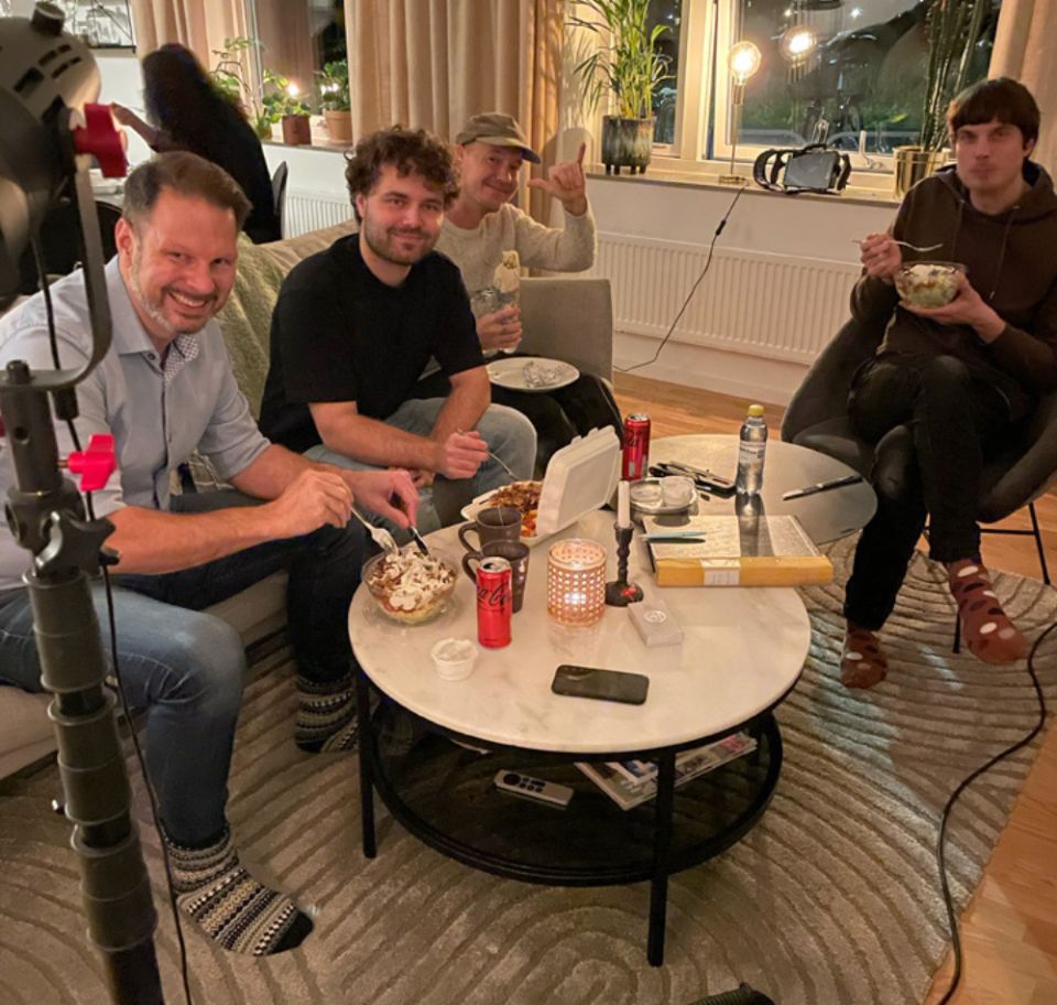 Bakom kulisserna-bild från en filminspelning där produktionsteamet sitter samlat i en soffa och äter mat under en paus.