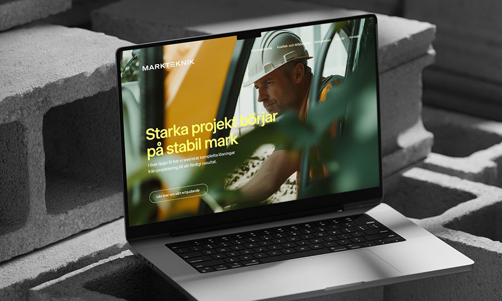  En bärbar dator som visar Marktekniks hemsida med rubriken ”Starka projekt börjar på stabil mark” över en bild av en anläggningsarbetare i hjälm.