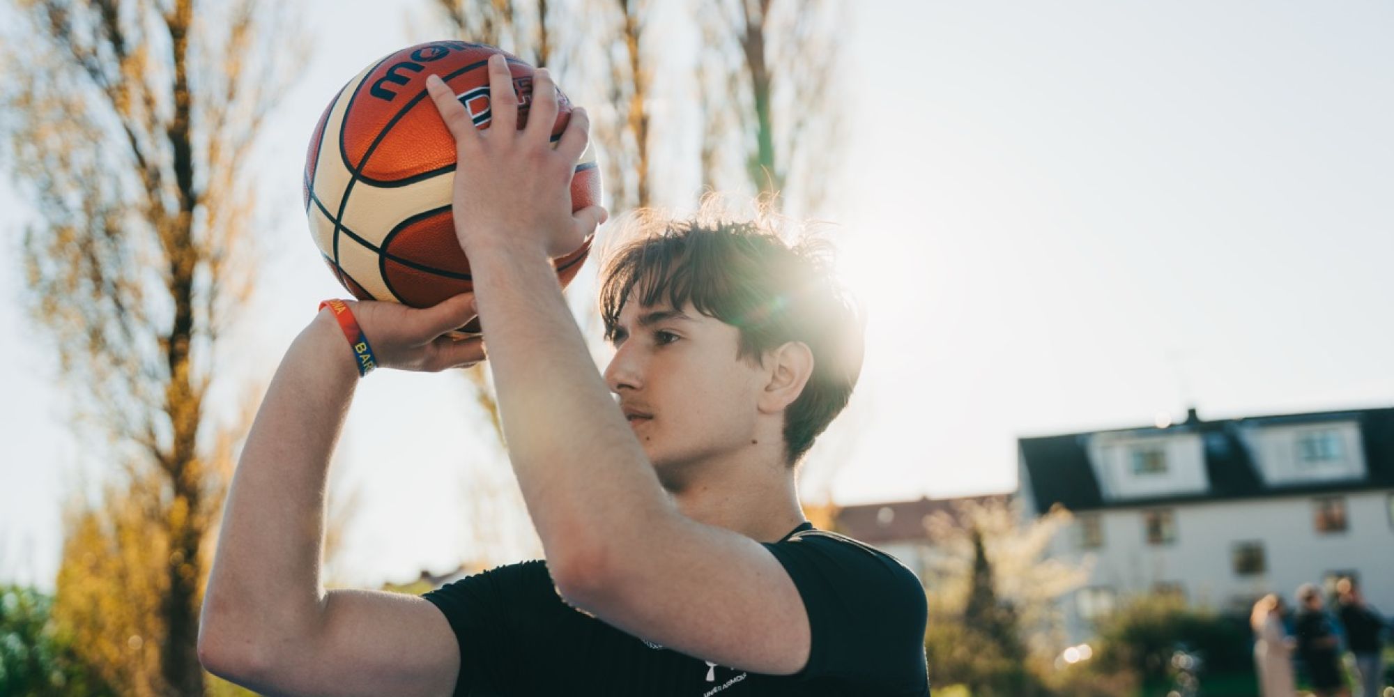 En ung kille siktar mot korgen med en basketboll på den utomhusplan som finansierats av Framtidsbanken, vilket visar på bankens bidrag till lokal livskvalitet och föreningsliv.