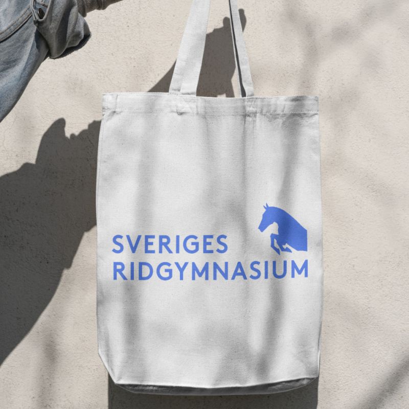  Tygkasse med Sveriges Ridgymnasiums logotyp hängande mot en ljus vägg.
