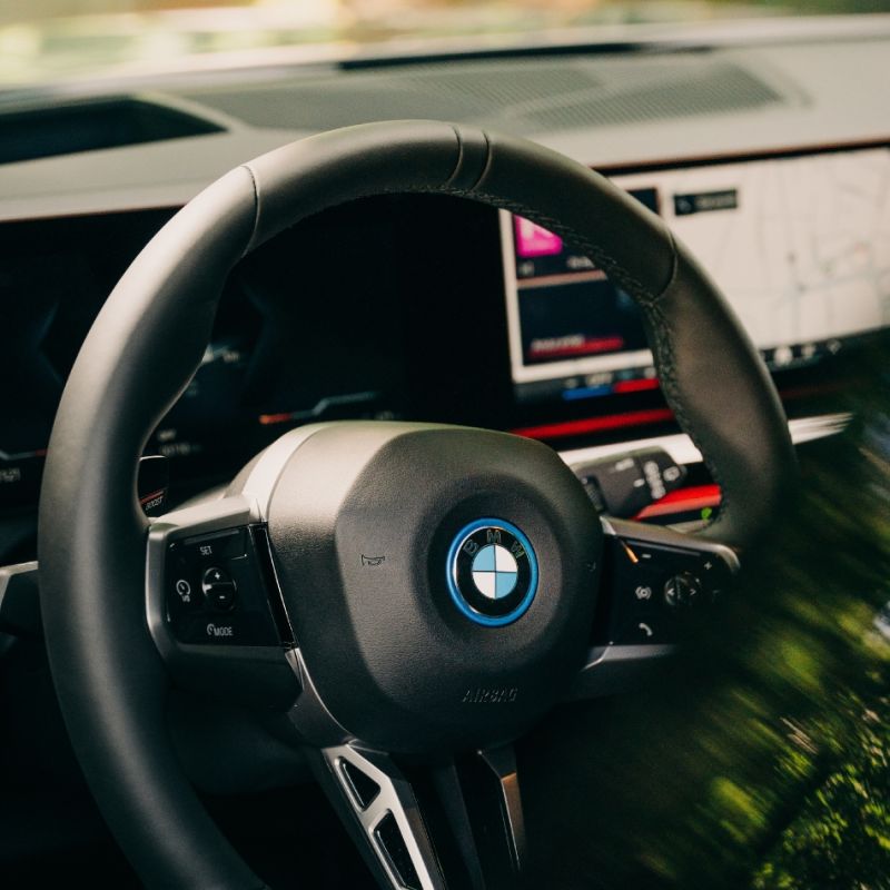 En närbild på förarplatsen i en BMW med fokus på ratten, logotypen och den digitala instrumentpanelen i bakgrunden.