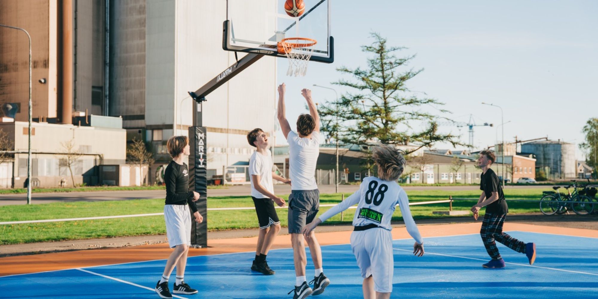  Ungdomar spelar basket på en färgglad utomhusplan som finansierats av Falkenbergs Sparbanks Framtidsbank, vilket främjar aktivitet och gemenskap i närområdet.