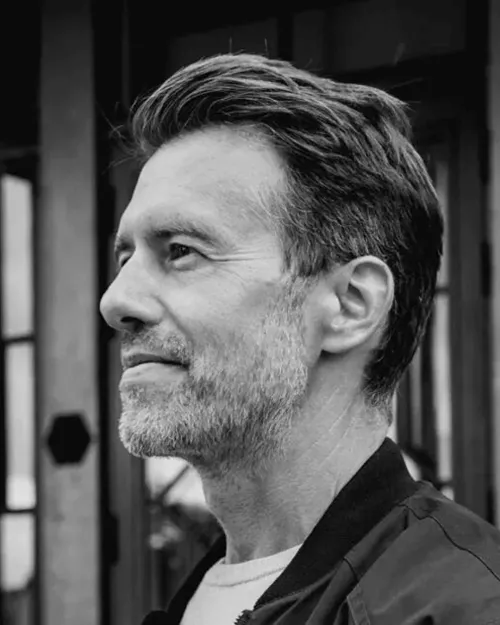 Svartvitt porträtt av Lars Sörqvist, VD, planner och delägare, i profil med skägg och bakåtkammat hår.