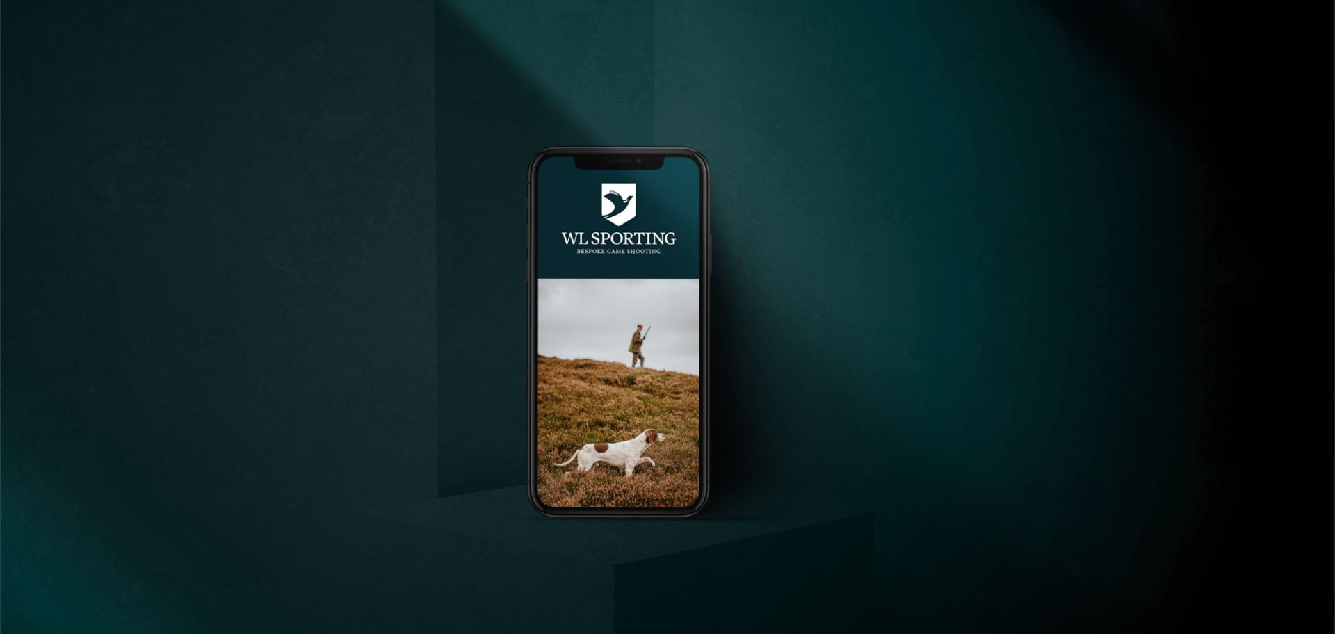  En smartphone placerad i en mörkgrön, skuggspelad miljö som visar WL Sportings hemsida med fokus på den naturnära grafiska profilen och företagets logotyp.