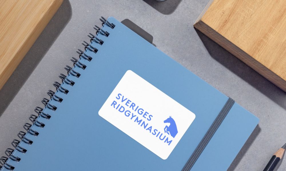 Blå anteckningsbok med Sveriges Ridgymnasiums logotyp på framsidan.