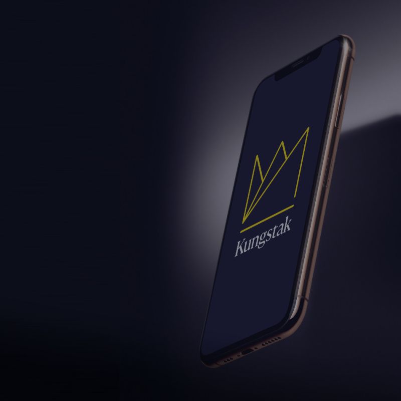  Smartphone som svävar i mörkret och visar Kungstaks nya logotyp på skärmen, vilket understryker företagets moderna digitala närvaro.