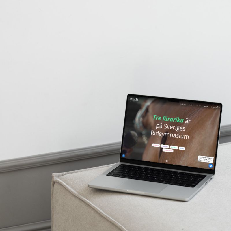 Bärbar dator som visar Sveriges Ridgymnasiums webbplats med texten "Tre lärorika år", placerad på en sittpuff.