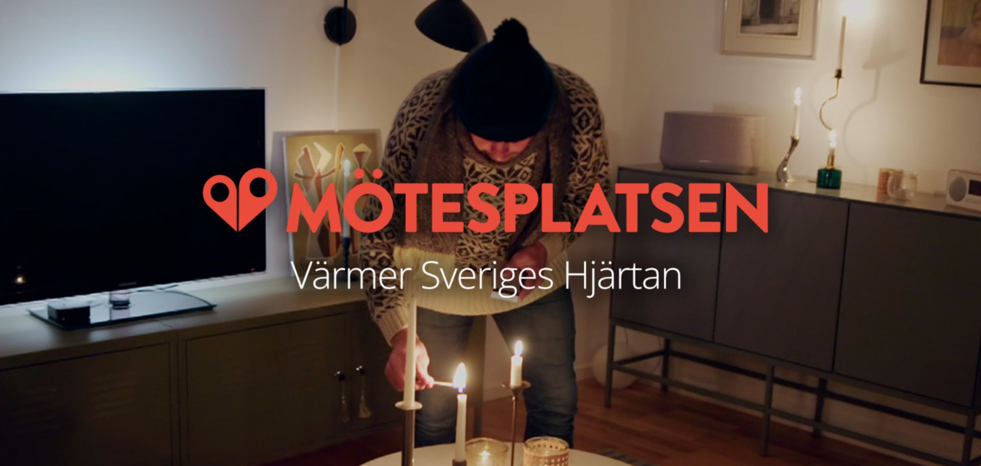 En man i stickad tröja och mössa tänder levande ljus i ett vardagsrum med logotypen för Mötesplatsen och texten "Värmer Sveriges Hjärtan" i förgrunden.