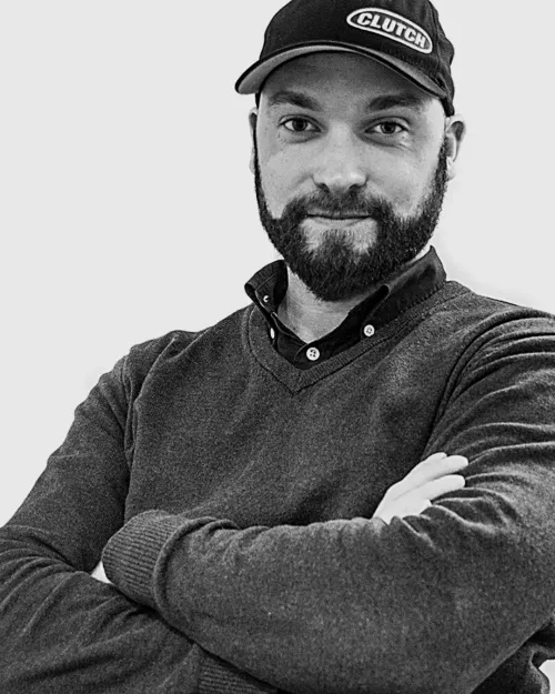 Porträtt av Claes Norin, webbutvecklare, med skägg och keps, armarna i kors och klädd i en mörk tröja.