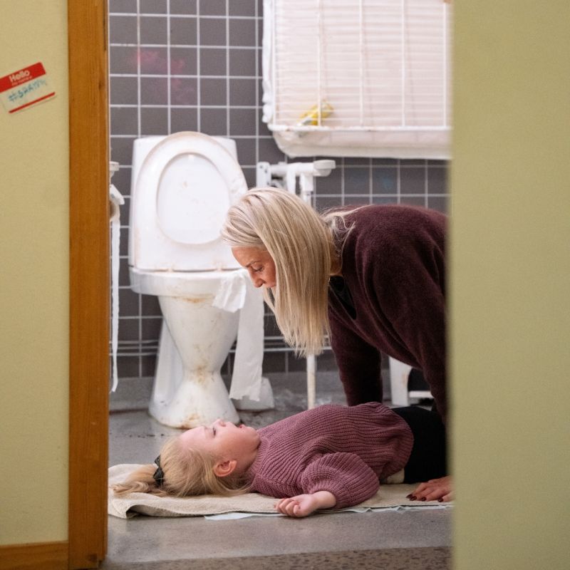 En stark bild från kampanjen som visar en kvinna som tvingas sköta omvårdnad av ett barn på ett toalettgolv, vilket illustrerar den akuta bristen på ordentligt anpassade faciliteter.