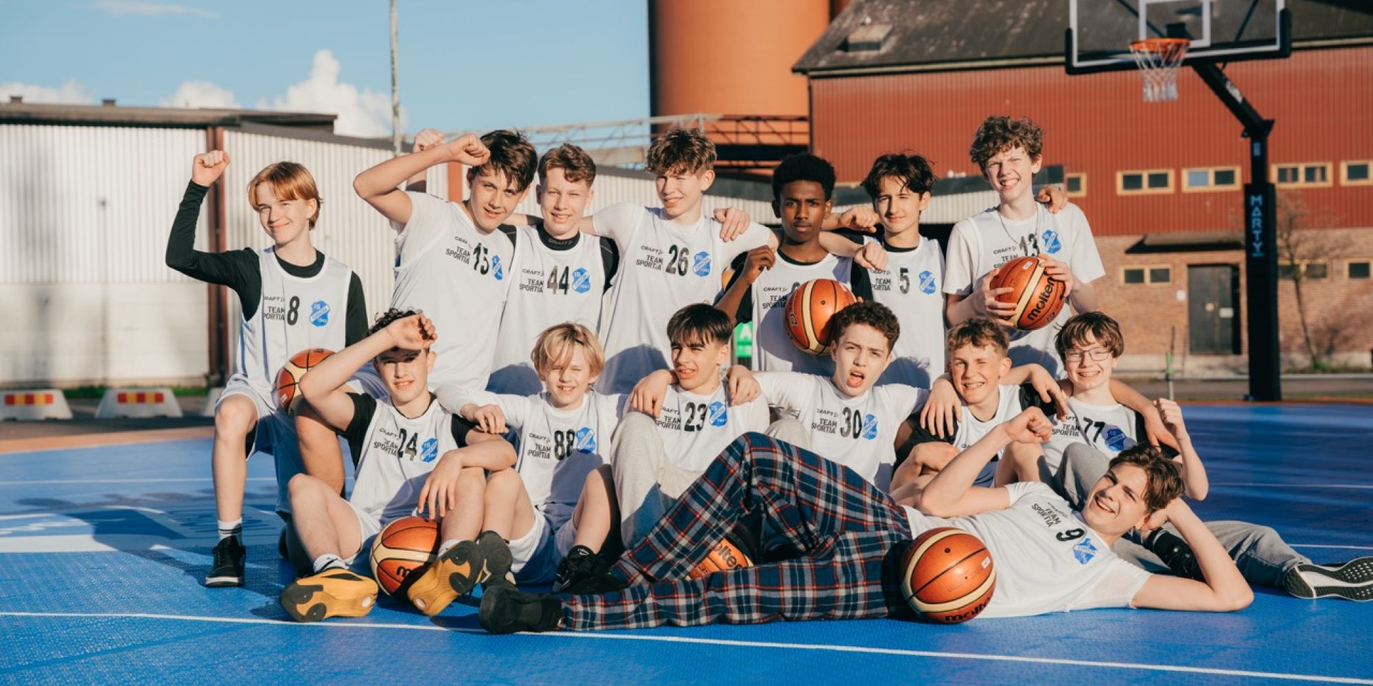 En gruppbild på basketlaget IS Orion som poserar glatt på sin nya utomhusplan, ett projekt som förverkligats med stöd från Falkenbergs Sparbanks Framtidsbank för att stärka det lokala föreningslivet.