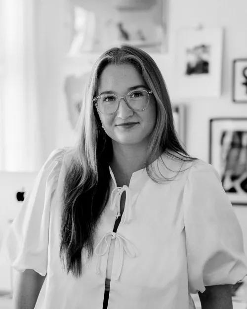 Porträtt av Moa Wennerberg, Social Media-ansvarig, med långt hår och glasögon, iklädd en vit blus.