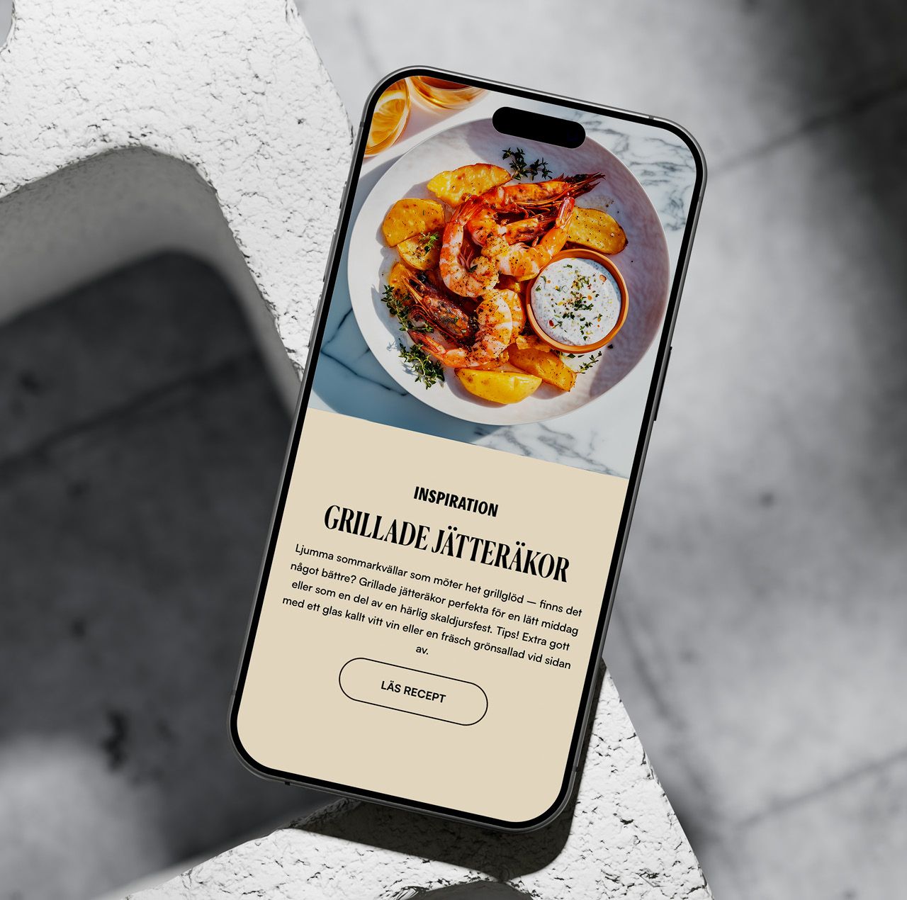 En smartphone som visar ett recept på grillade jätteräkor från Fisk Direkts hemsida, med en inspirerande matbild och en knapp för att läsa hela receptet.