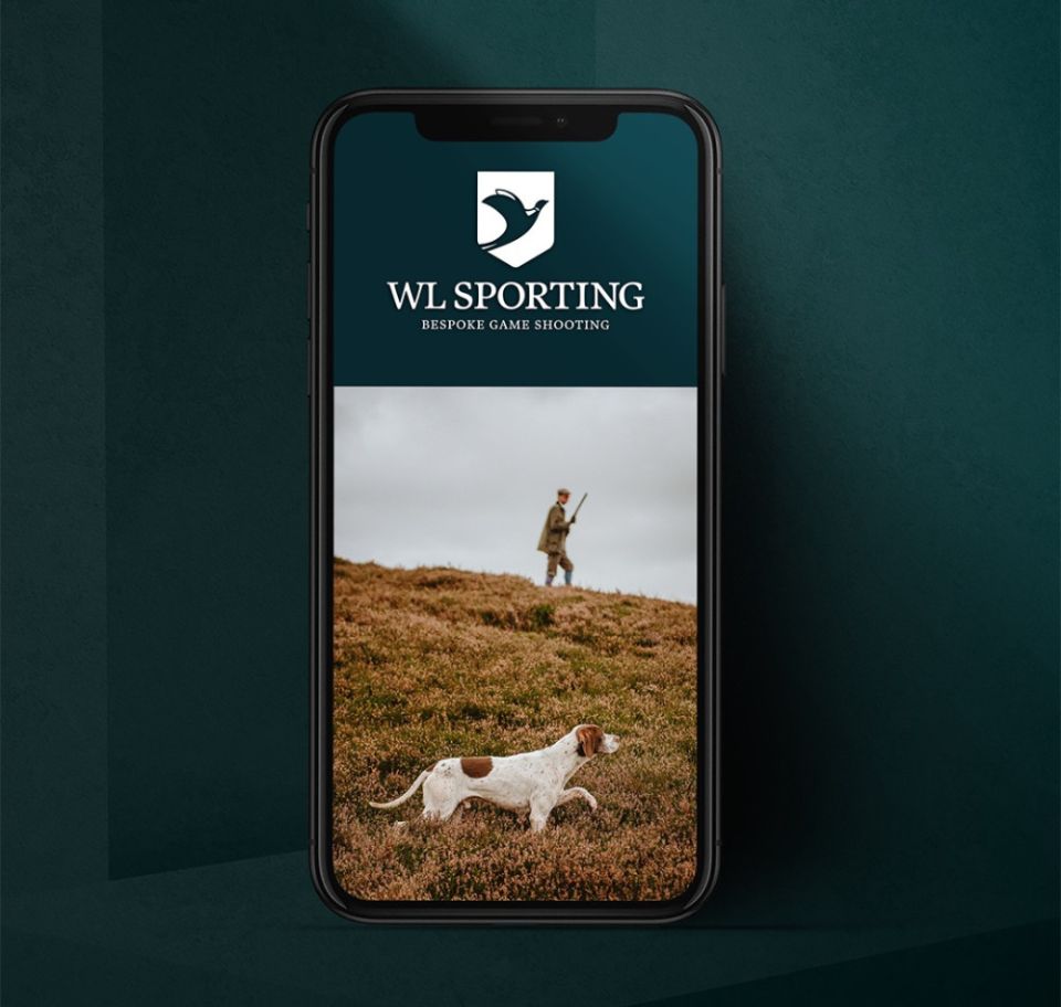 En smartphone som visar WL Sportings hemsida i mobilversion, med företagets logotyp i vitt mot en mörkgrön bakgrund över en bild på en jägare och en jakthund i ett öppet landskap.