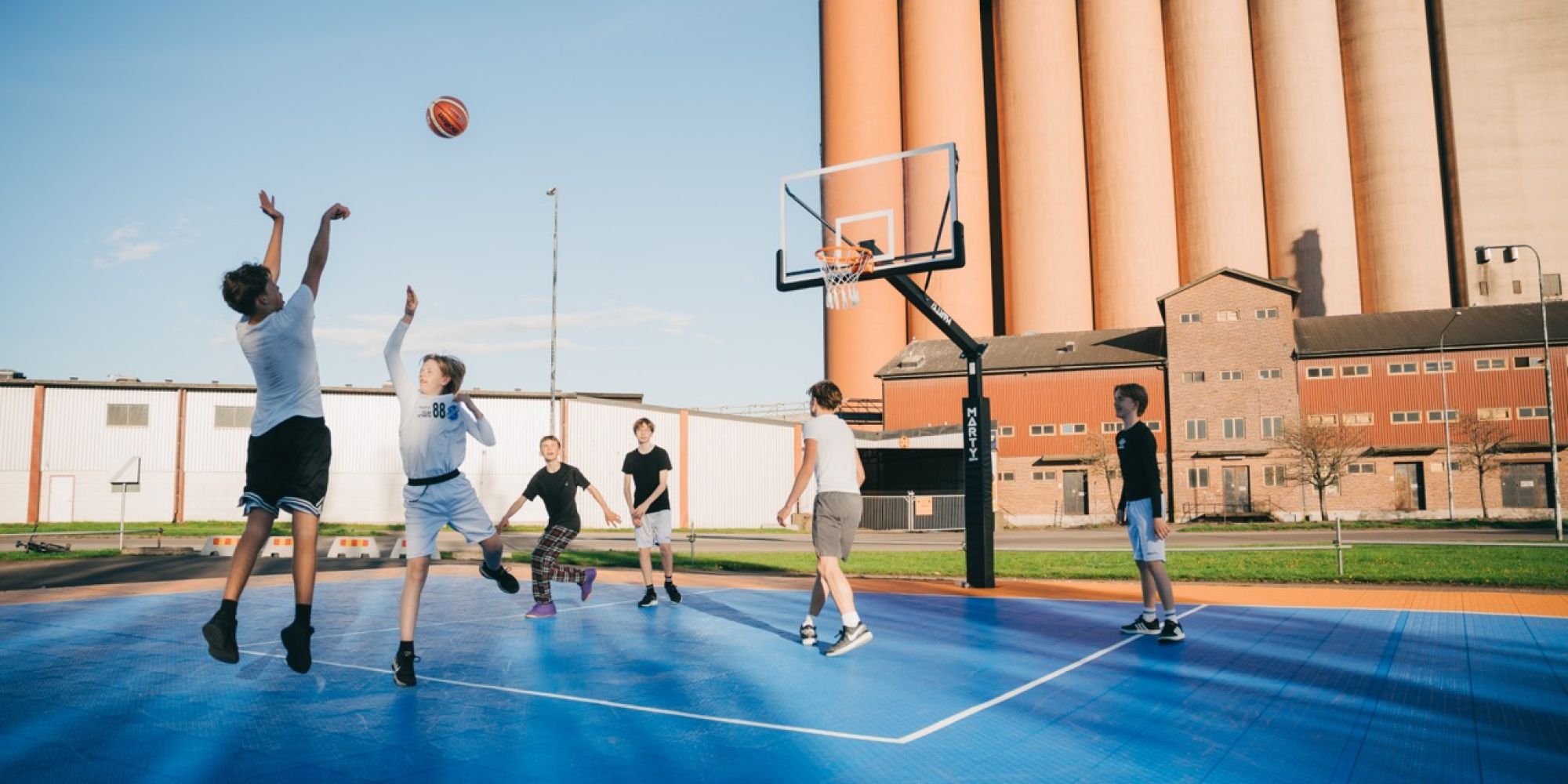 Ungdomar spelar basket på en utomhusplan i Falkenberg, ett projekt möjliggjort genom stöd från Falkenbergs Sparbanks Framtidsbank för att främja lokal rörelse och livskvalitet.