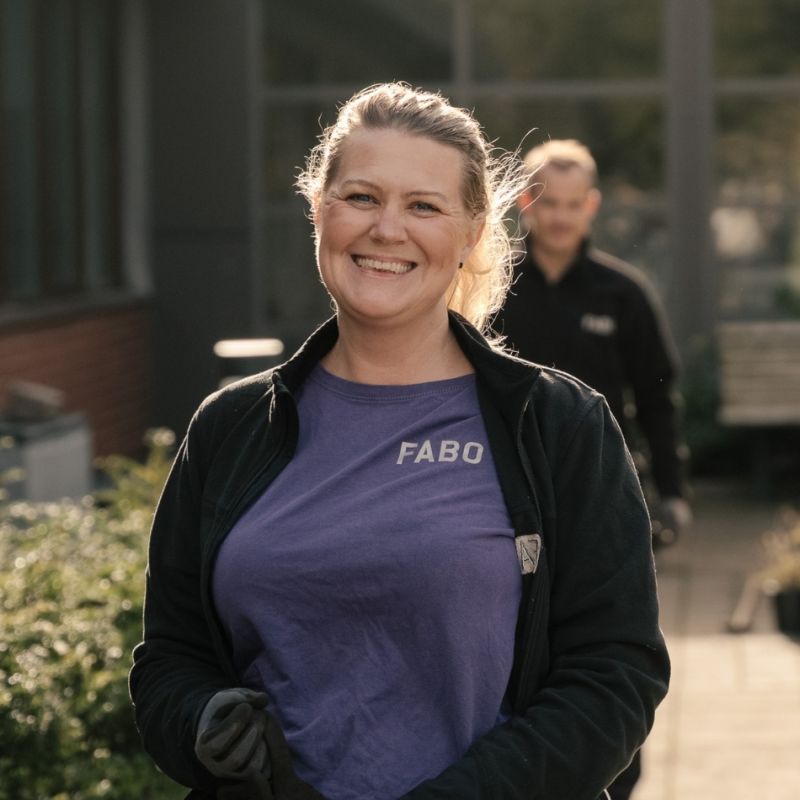 En glad och engagerad medarbetare från Fabo i profilkläder, fotograferad utomhus för att lyfta fram den mänskliga närvaron i organisationens vardagliga arbete.