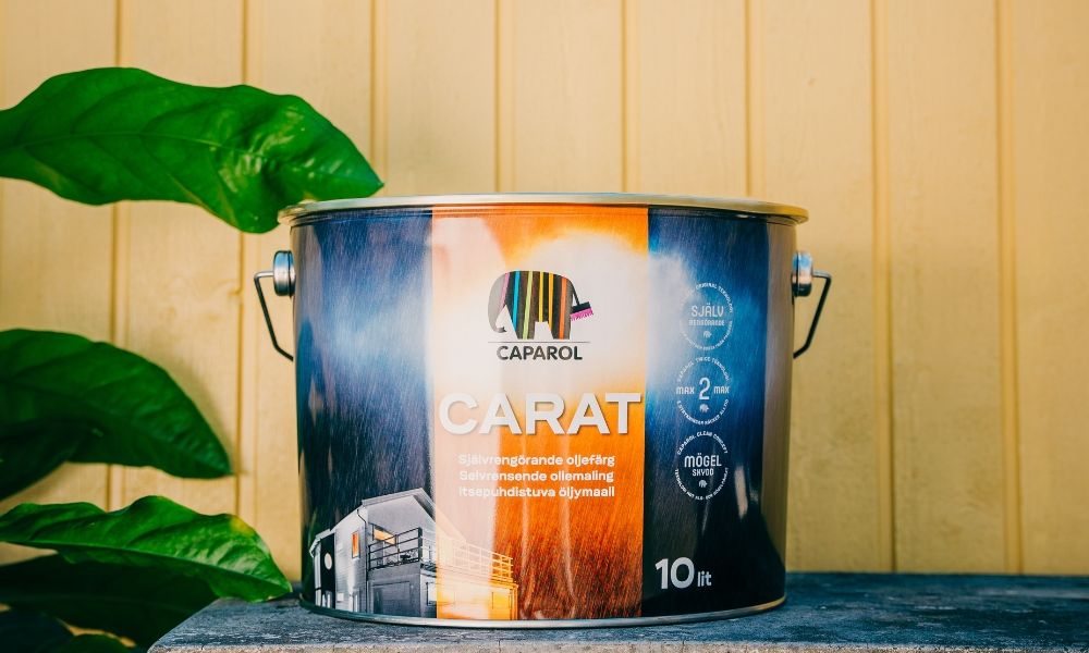 Färgburk med Caparol Carat självrengörande oljefärg framför en gulmålad trävägg.
