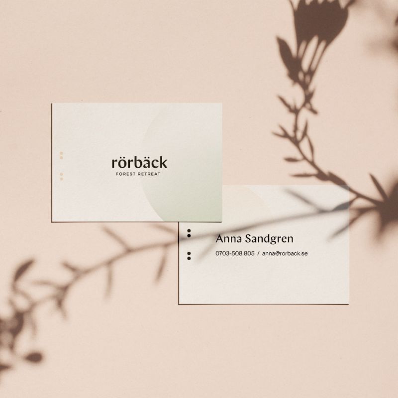  Visitkort för Rörbäck Forest Retreat och Anna Sandgren, presenterade på en ljusrosa yta med mjuka skuggor från en växt.