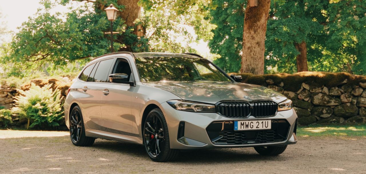  En silverfärgad BMW kombi parkerad på en grusplan framför en lummig trädgård och en stenmur, vilket illustrerar Lunds Bils arbete med högkvalitativt content.
