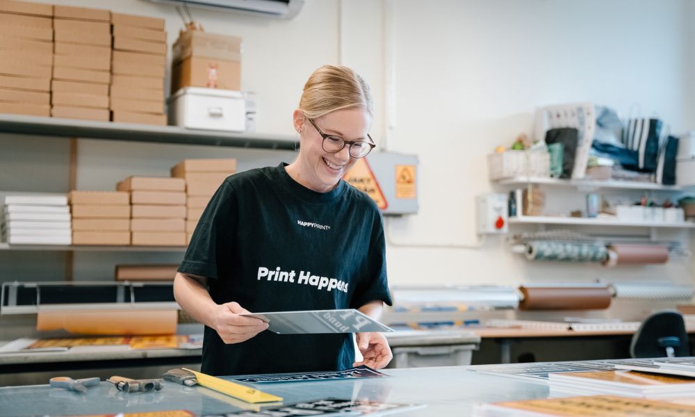 Leende kvinna som granskar tryckta skyltar i Happy Prints verkstad.