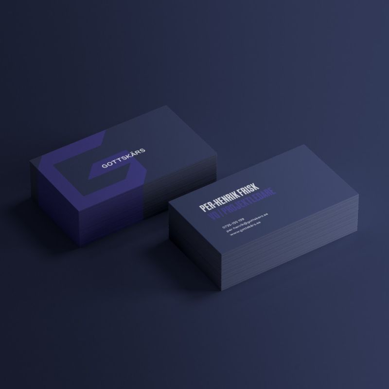 Två travar med mörkblå visitkort för Gottskärs. Ena sidan visar företagets logotyp i en lila nyans mot den mörka bakgrunden, medan den andra sidan visar kontaktuppgifter för en vd och projektledare med tydlig, modern typografi.