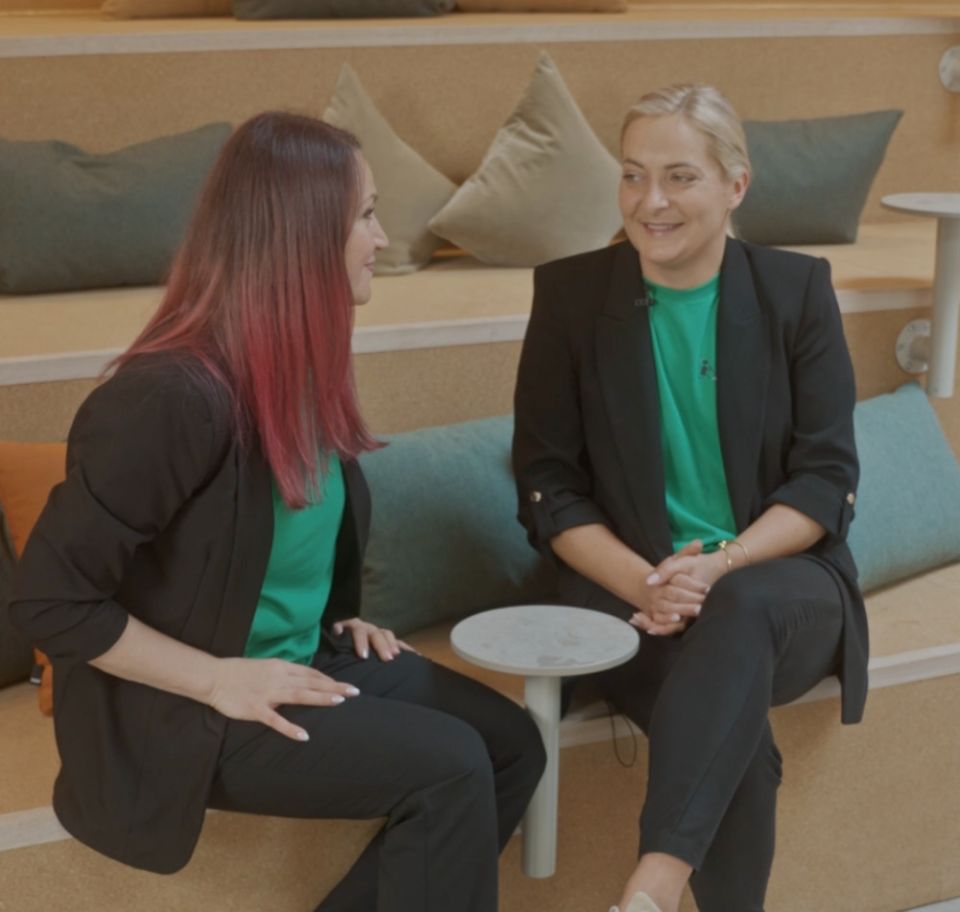 Katarina och Sabina sitter i en trappliknande sittmöbel i en kontorsmiljö och samtalar. Båda bär svarta kavajer över gröna profil-t-shirts och ser glada och engagerade ut inför uppstarten i Göteborg.
