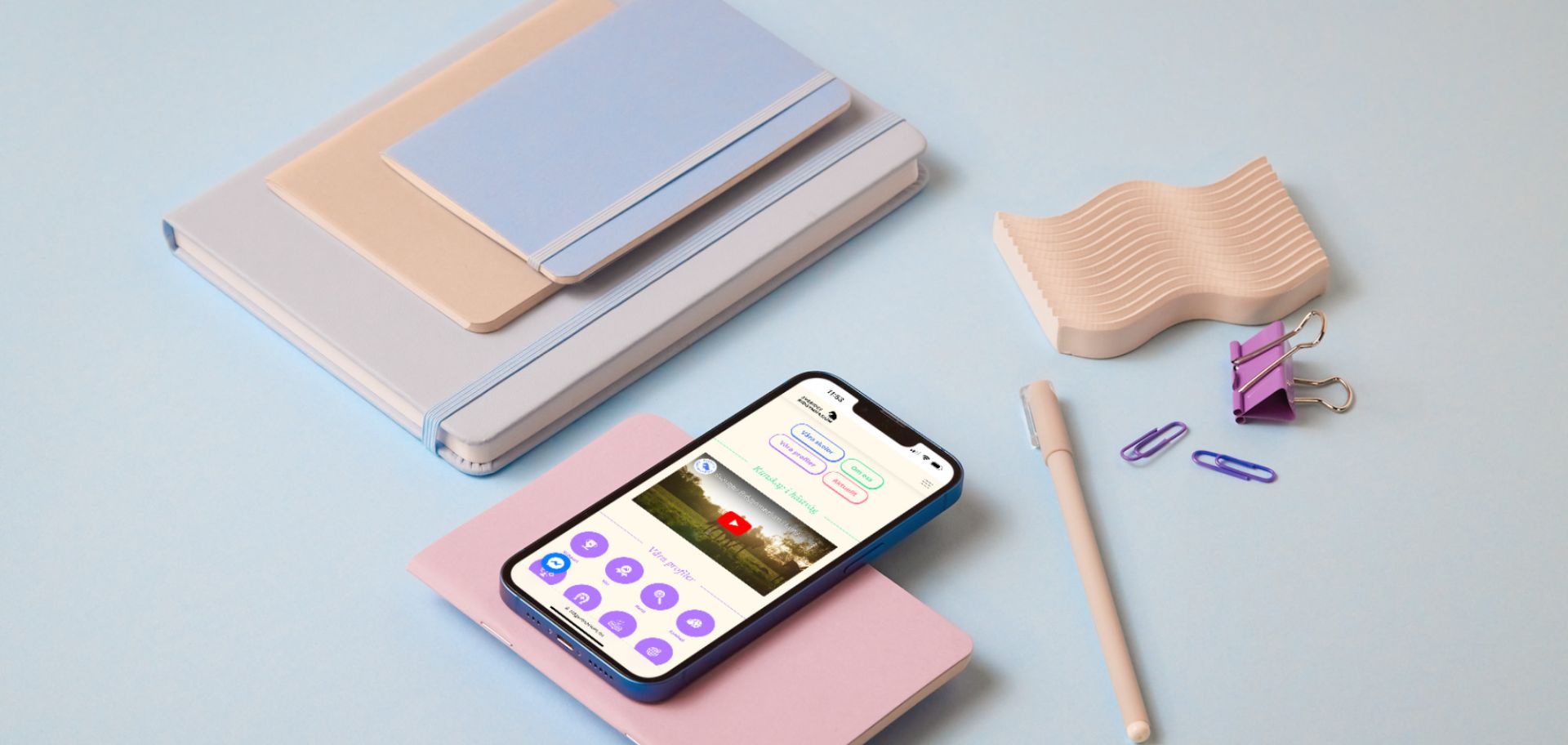 Mobiltelefon som visar Sveriges Ridgymnasiums hemsida, placerad bland anteckningsblock och pennor.