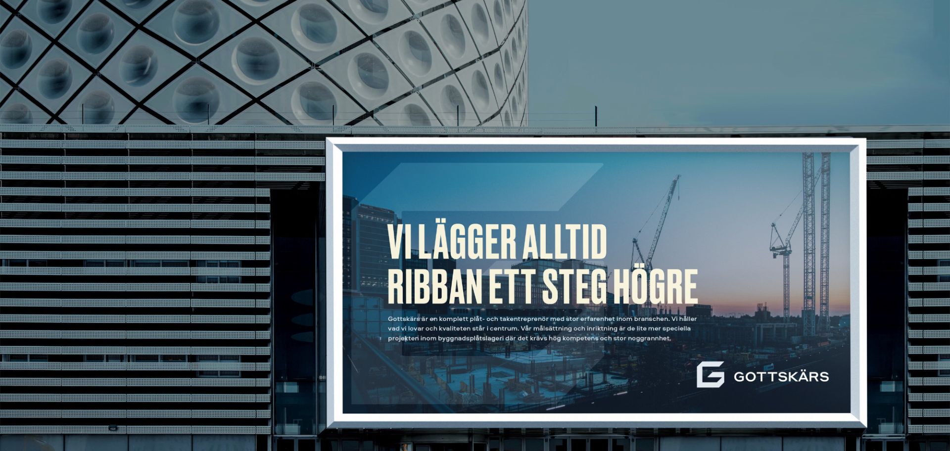 En stor reklamskylt på en modern byggnad visar Gottskärs visuella identitet. Skylten har rubriken ”Vi lägger alltid ribban ett steg högre” mot en bakgrund av en byggarbetsplats i skymning, vilket förmedlar företagets ambition och kompetens inom plåt- och takentreprenad.
